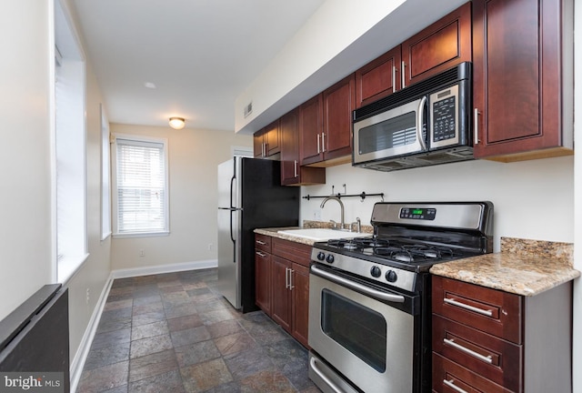 kitchen with baseboards, visible vents, stone finish floor, appliances with stainless steel finishes, and a sink