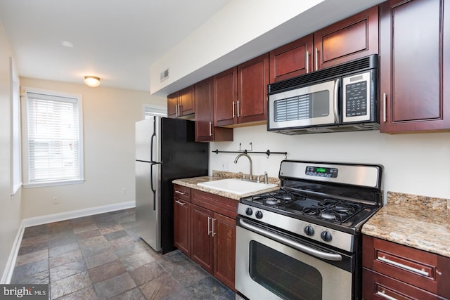 kitchen featuring stainless steel appliances, visible vents, stone finish flooring, a sink, and baseboards