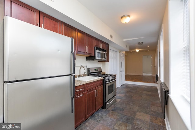 kitchen featuring baseboards, stone finish flooring, stainless steel appliances, light countertops, and a sink