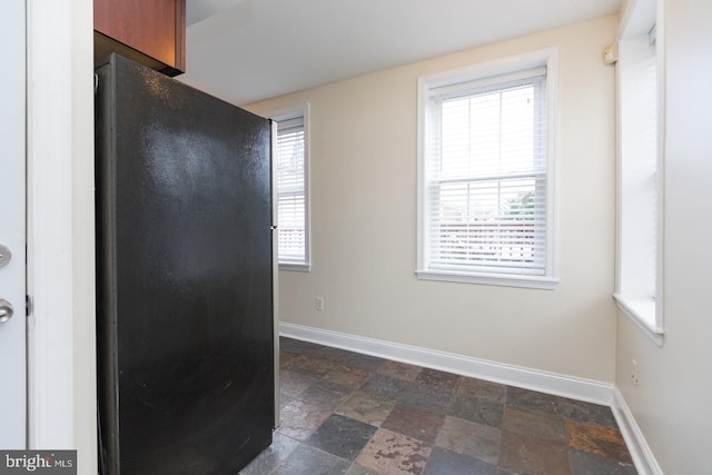 spare room with plenty of natural light, stone finish flooring, and baseboards