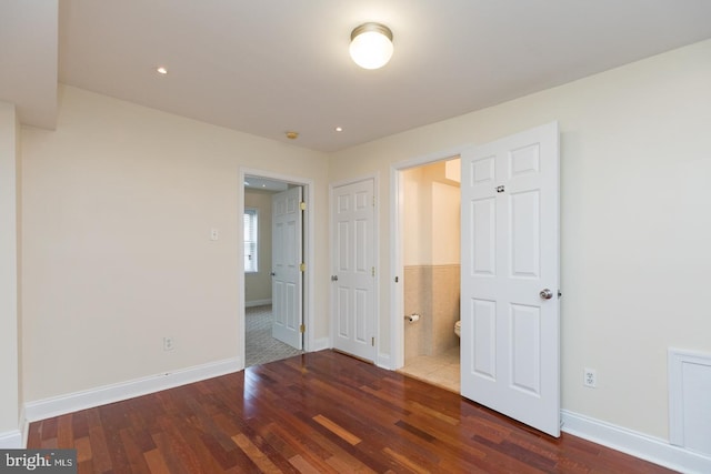 unfurnished bedroom with ensuite bath, wood finished floors, and baseboards