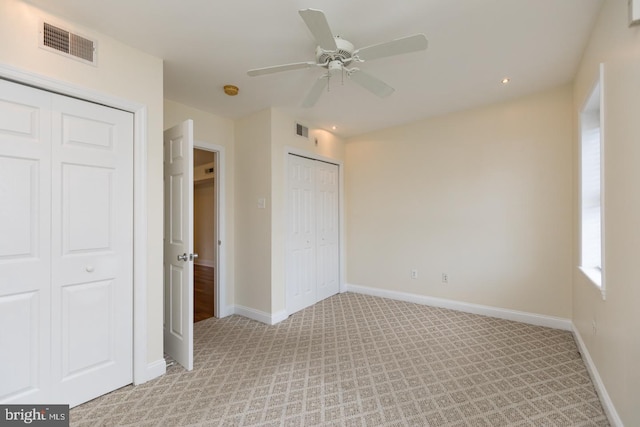 unfurnished bedroom featuring light carpet, two closets, visible vents, and baseboards