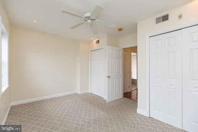 unfurnished bedroom featuring baseboards, visible vents, multiple closets, and light colored carpet