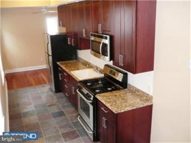 kitchen with reddish brown cabinets, appliances with stainless steel finishes, light stone counters, and baseboards