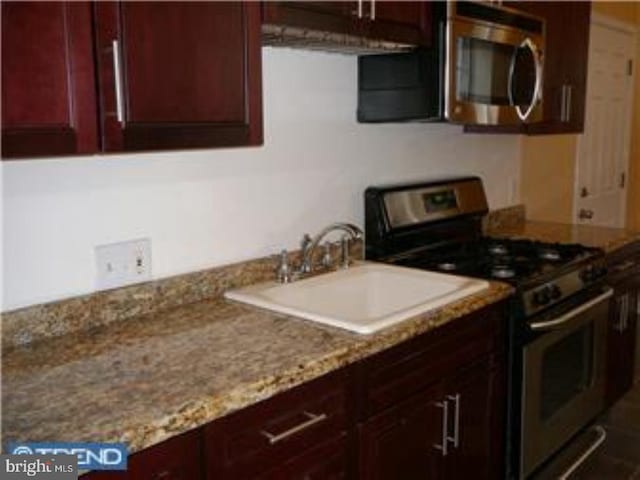 kitchen featuring reddish brown cabinets, appliances with stainless steel finishes, a sink, and light stone counters