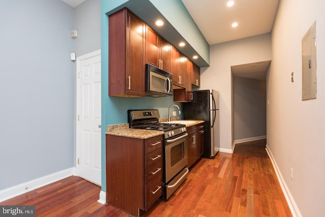 kitchen with baseboards, electric panel, appliances with stainless steel finishes, and wood finished floors