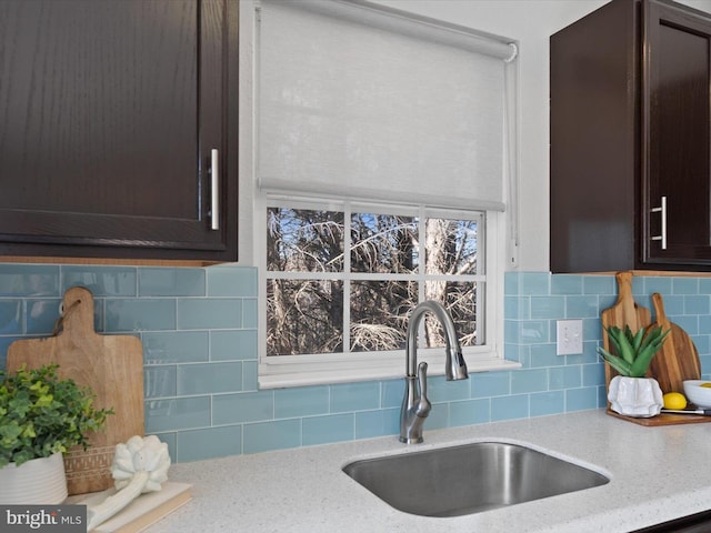 kitchen with a sink, light stone countertops, backsplash, and dark brown cabinets