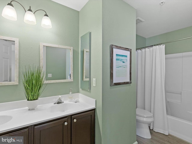 bathroom featuring visible vents, toilet, double vanity, wood finished floors, and a sink