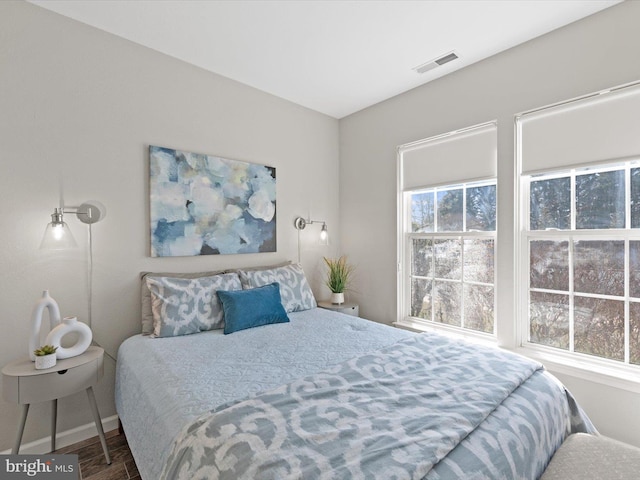 bedroom featuring visible vents, multiple windows, baseboards, and wood finished floors