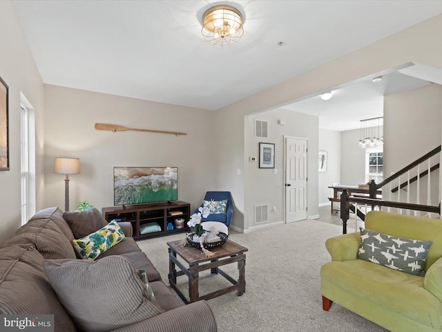 carpeted living room featuring visible vents, baseboards, a notable chandelier, and stairway