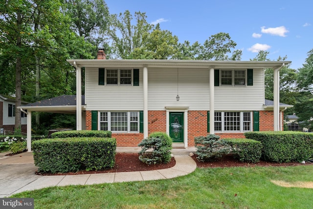 view of front of home featuring an attached carport, brick siding, concrete driveway, a front lawn, and a chimney