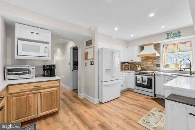 kitchen with white appliances, light wood finished floors, custom exhaust hood, a sink, and decorative backsplash