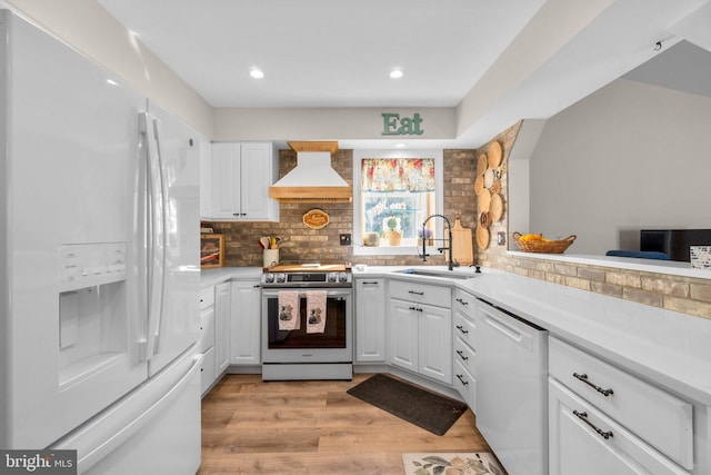 kitchen featuring white appliances, white cabinetry, custom range hood, and a sink