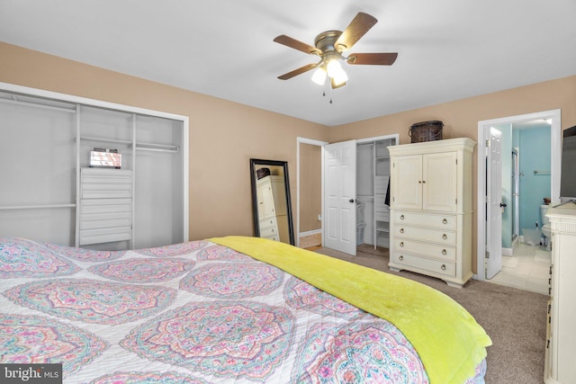 bedroom featuring ensuite bath, carpet flooring, two closets, and ceiling fan