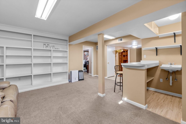 finished basement with light colored carpet, baseboards, visible vents, and a sink