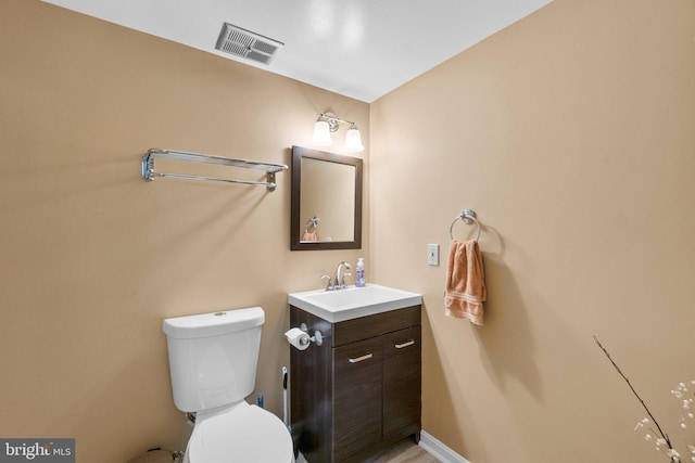 half bath with vanity, toilet, baseboards, and visible vents