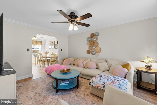 living room featuring wood finished floors, baseboards, arched walkways, ceiling fan, and crown molding