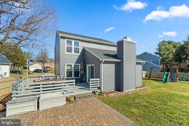 back of property with a playground, fence, roof with shingles, a lawn, and a chimney