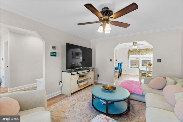 living area featuring baseboards, arched walkways, light wood-style floors, and ornamental molding