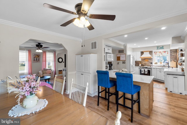 dining room featuring crown molding, light wood-style flooring, visible vents, and arched walkways