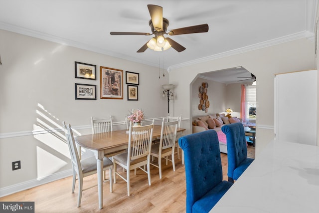 dining area featuring arched walkways, ornamental molding, a ceiling fan, and light wood finished floors