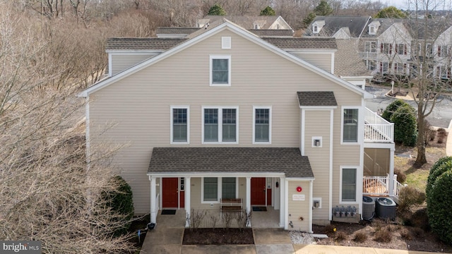 traditional-style house with a porch, roof with shingles, and cooling unit