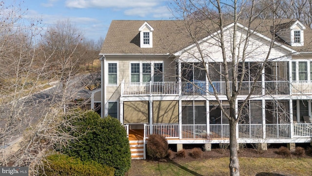 rear view of house featuring a shingled roof, a sunroom, and a balcony