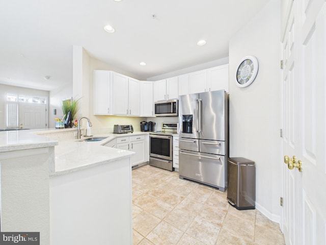 kitchen featuring light stone counters, stainless steel appliances, white cabinets, a sink, and a peninsula