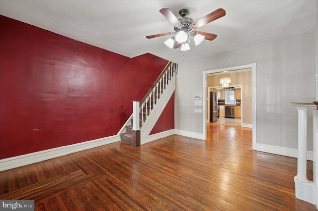 spare room with ceiling fan with notable chandelier, stairway, wood finished floors, and baseboards