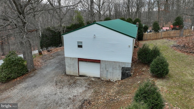 view of outbuilding with a garage, driveway, an outbuilding, and fence