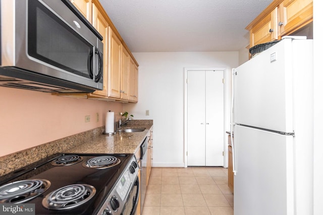 kitchen with light tile patterned floors, light brown cabinetry, a sink, appliances with stainless steel finishes, and a textured ceiling