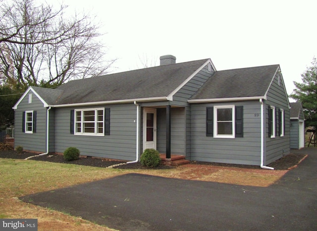 ranch-style house featuring a shingled roof, a front yard, and a chimney