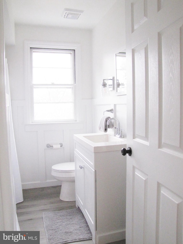 bathroom with visible vents, a wainscoted wall, toilet, a decorative wall, and vanity