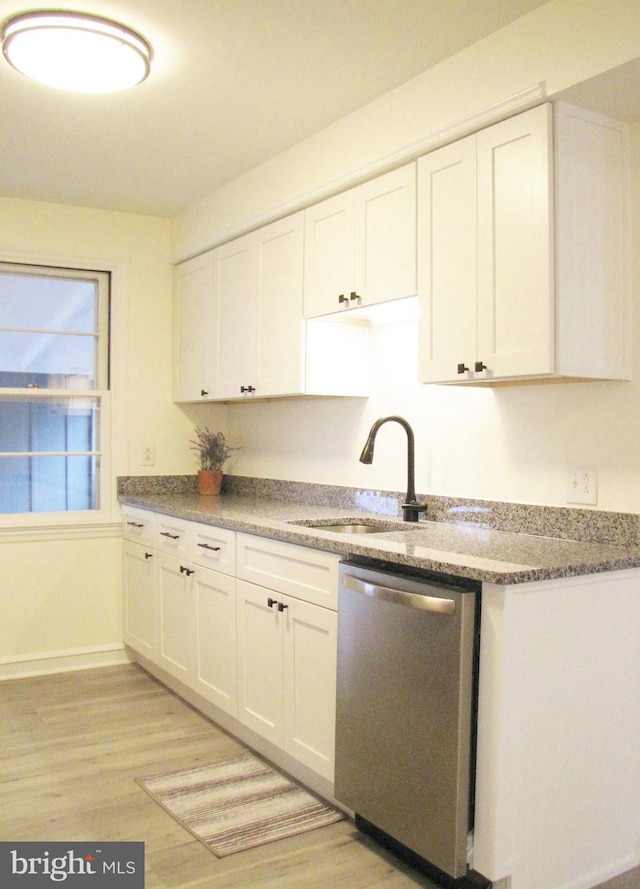 kitchen with a sink, light wood finished floors, stainless steel dishwasher, and white cabinetry