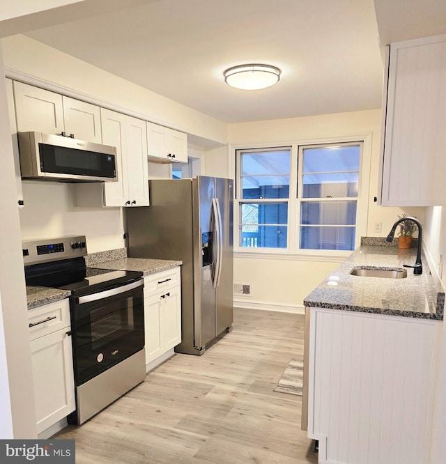 kitchen with visible vents, a sink, white cabinetry, stainless steel appliances, and light wood-style floors