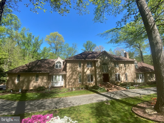 view of front of home with brick siding, a chimney, and a front lawn
