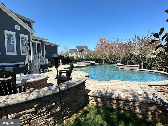 outdoor pool with a patio area, fence, a fire pit, and an in ground hot tub