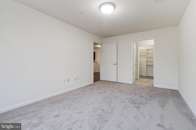 unfurnished bedroom with carpet floors, a walk in closet, and baseboards