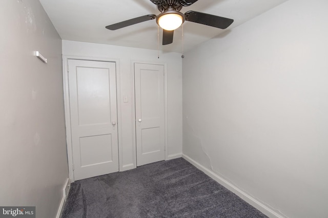 unfurnished bedroom with a ceiling fan, dark colored carpet, and baseboards