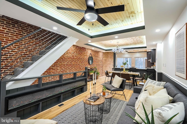 living area with brick wall, wood finished floors, wood ceiling, a tray ceiling, and an inviting chandelier