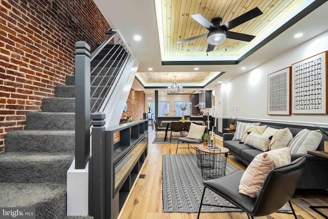 living room featuring wooden ceiling, brick wall, stairs, a tray ceiling, and light wood-type flooring