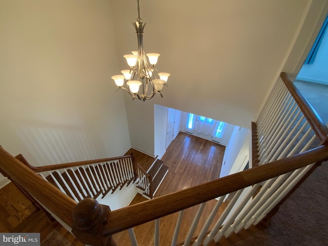 stairs with a notable chandelier, a high ceiling, and wood finished floors