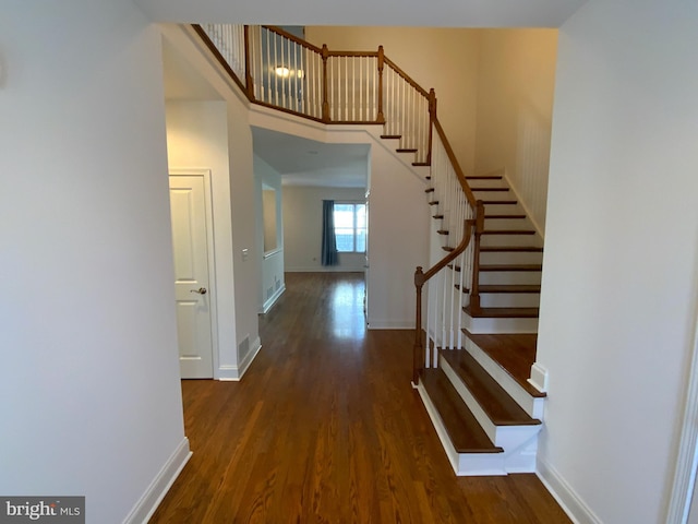 foyer entrance featuring stairway, baseboards, wood finished floors, and a towering ceiling