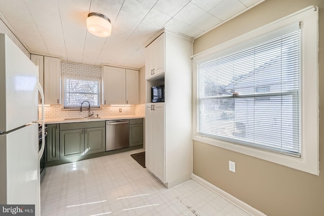 kitchen with a sink, stainless steel dishwasher, freestanding refrigerator, light countertops, and light floors