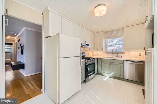 kitchen with green cabinets, under cabinet range hood, light countertops, stainless steel appliances, and a sink