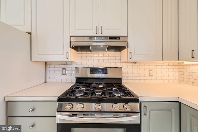 kitchen with light countertops, white cabinets, under cabinet range hood, gas range, and tasteful backsplash