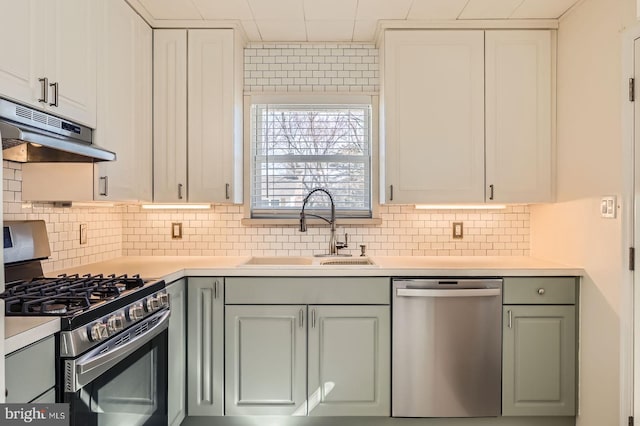 kitchen with under cabinet range hood, appliances with stainless steel finishes, light countertops, and a sink