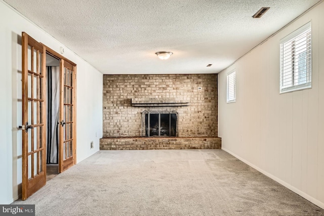 unfurnished living room with visible vents, a textured ceiling, a brick fireplace, and carpet flooring