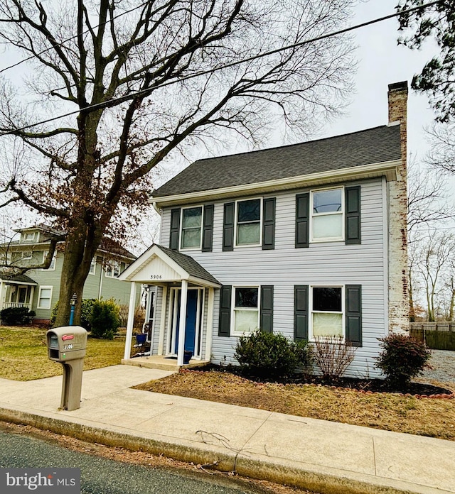 colonial-style house featuring a chimney and roof with shingles