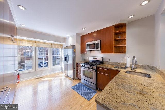 kitchen with a sink, open shelves, light stone counters, stainless steel appliances, and light wood finished floors